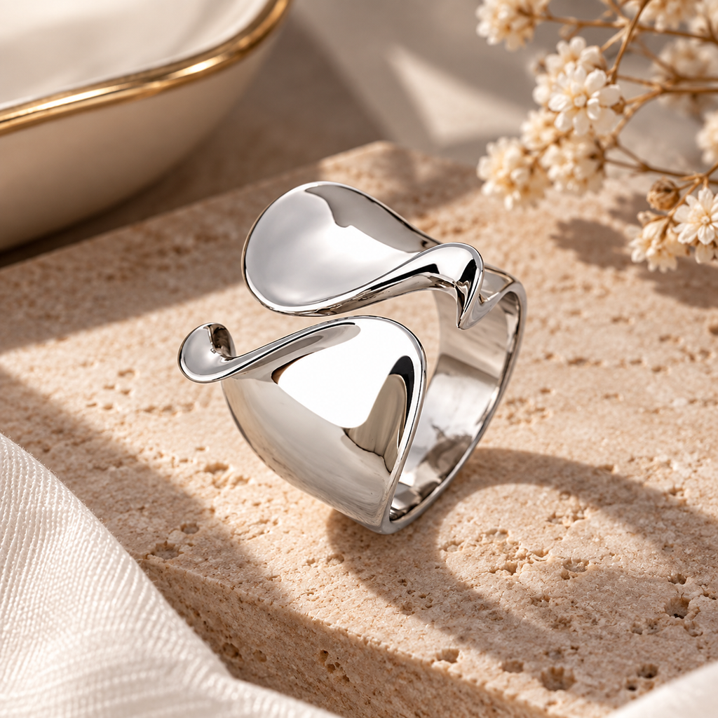 Silberfarbener Statement-Ring auf einer Steinplatte neben Trockenblumen